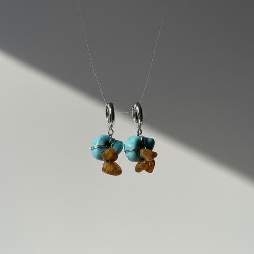 Pair of earrings with turquoise and amber beads on a gray background