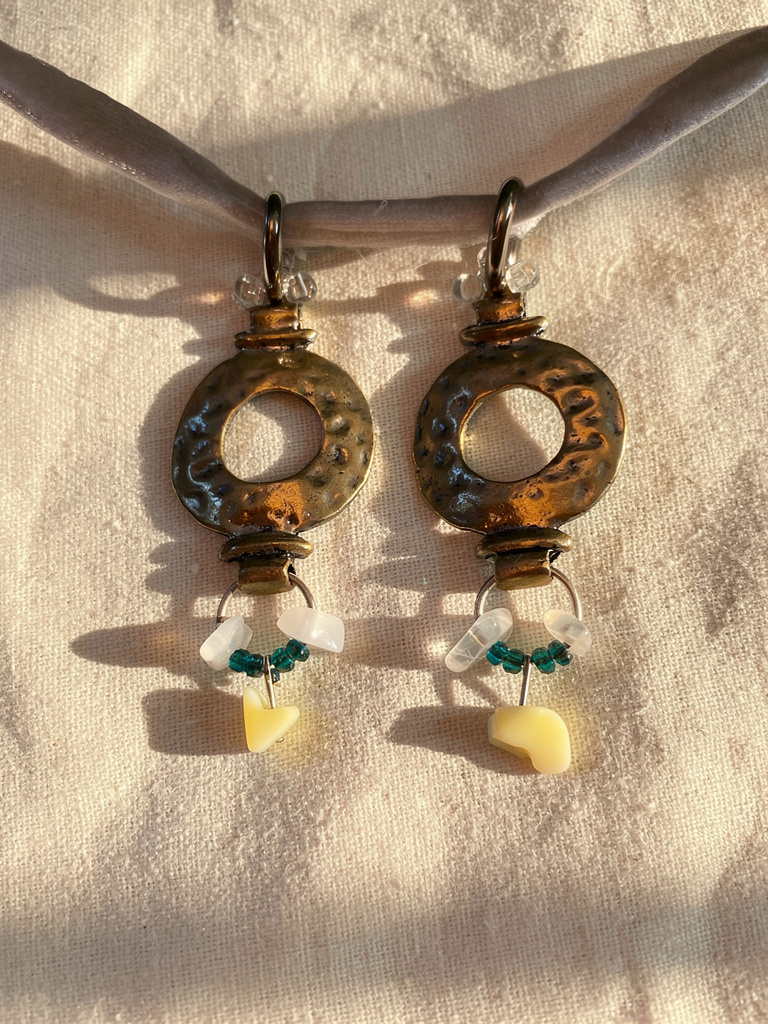 Pair of silver earrings with white and green beads on a beige fabric background