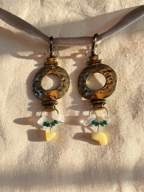 Pair of silver earrings with white and green beads on a beige fabric background