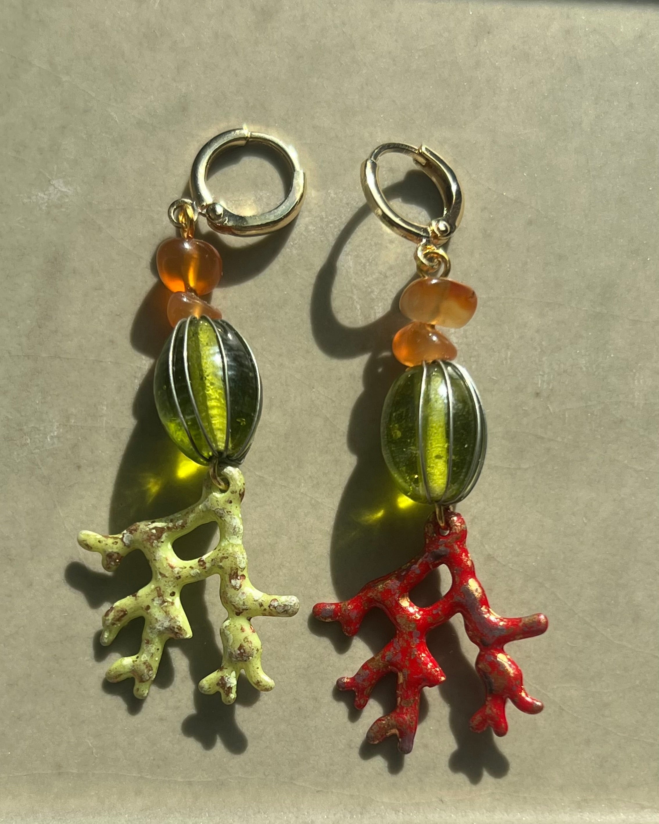 Pair of earrings with coral and bead charms on a neutral background