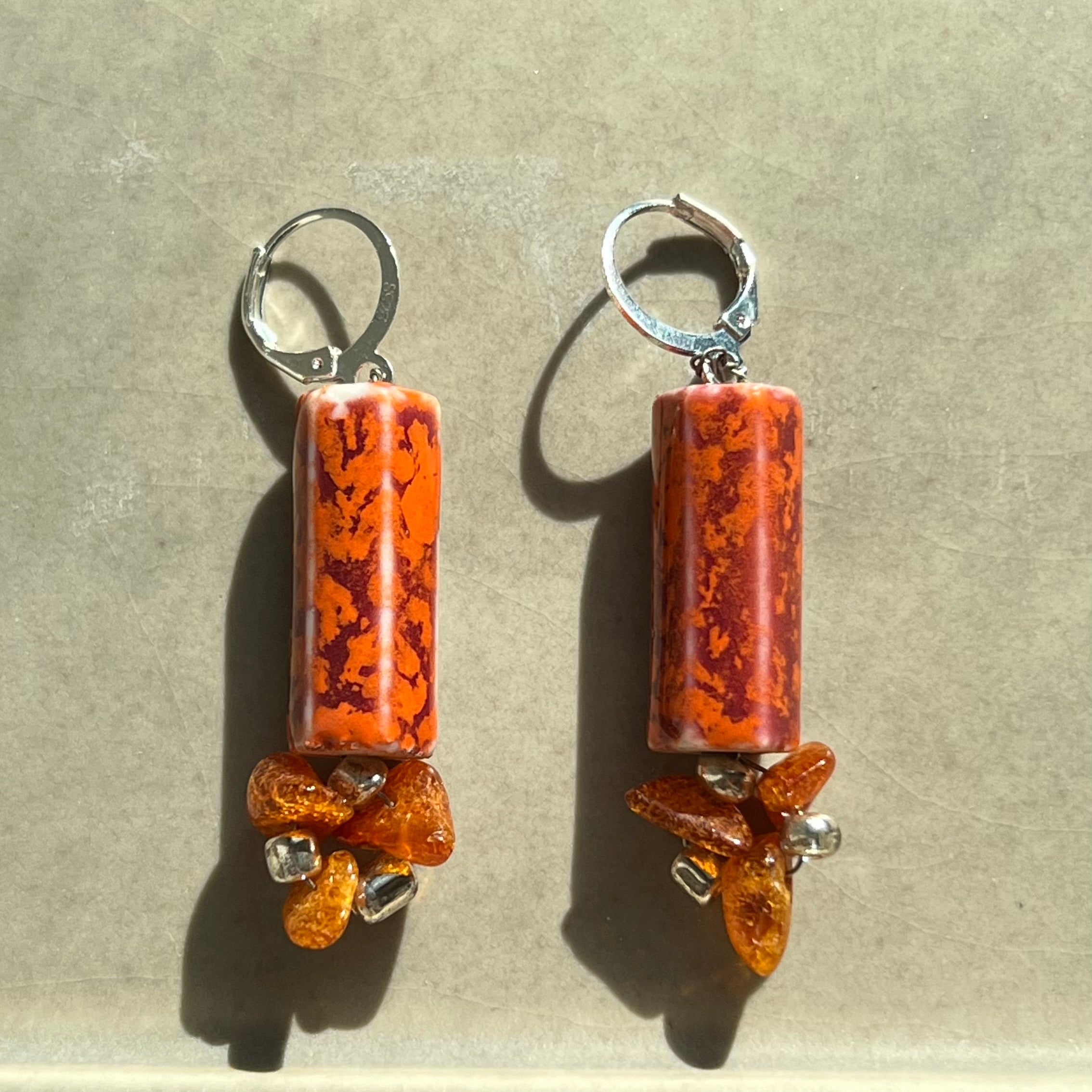 Pair of orange cylindrical earrings with silver hooks on a gray background
