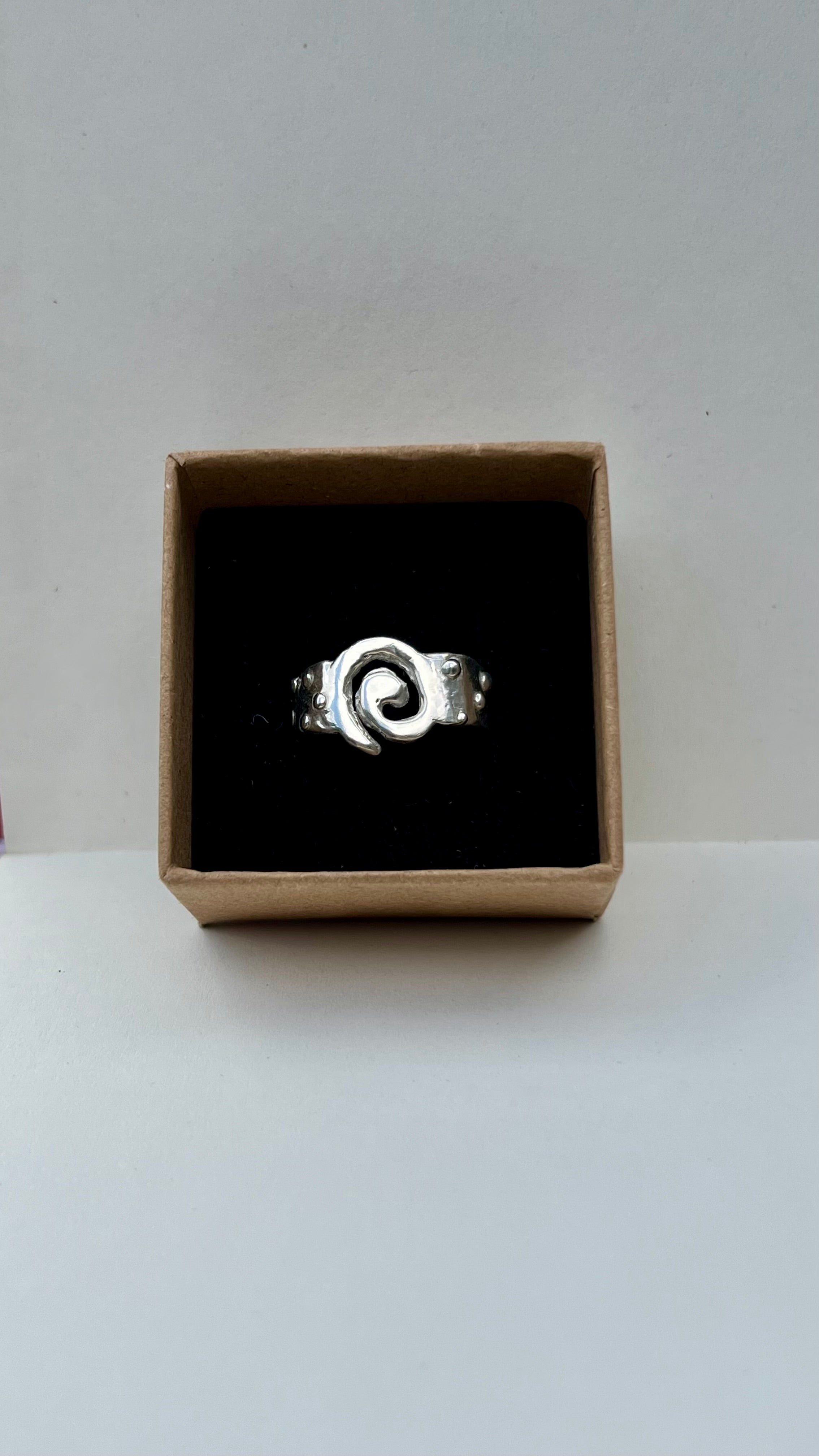 Silver ring with a spiral design in a cardboard box on a white background