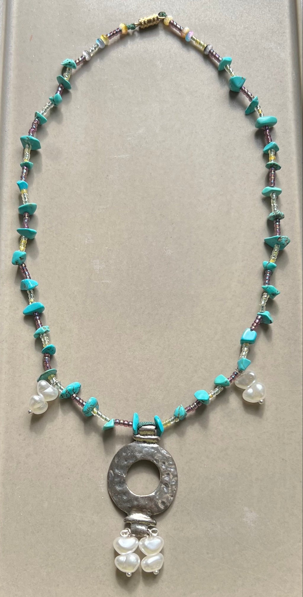 Necklace with beads and a central pendant on a gray card