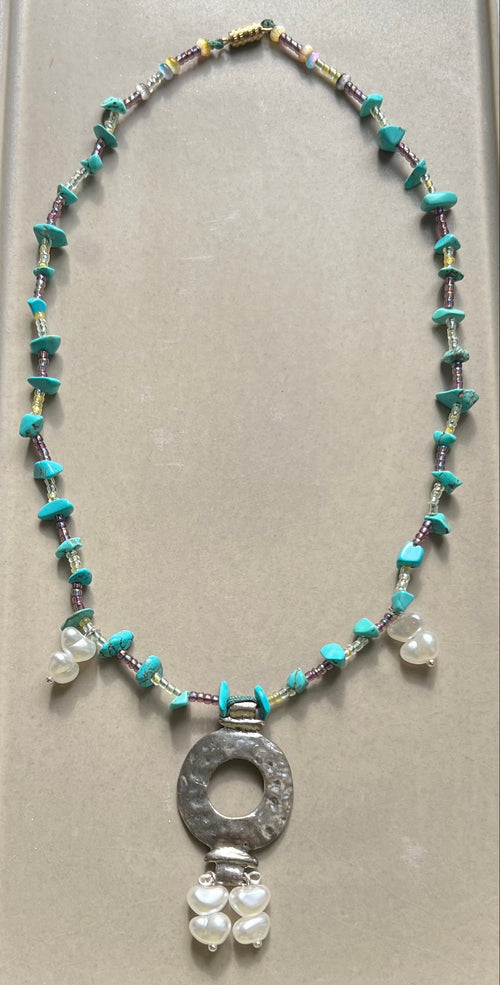 Necklace with beads and a central pendant on a gray card