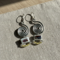 Silver spiral earrings with square charms on a textured fabric background