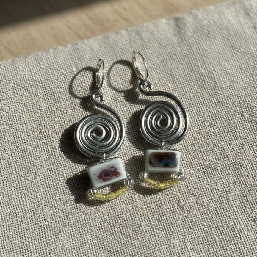 Silver spiral earrings with square charms on a textured fabric background