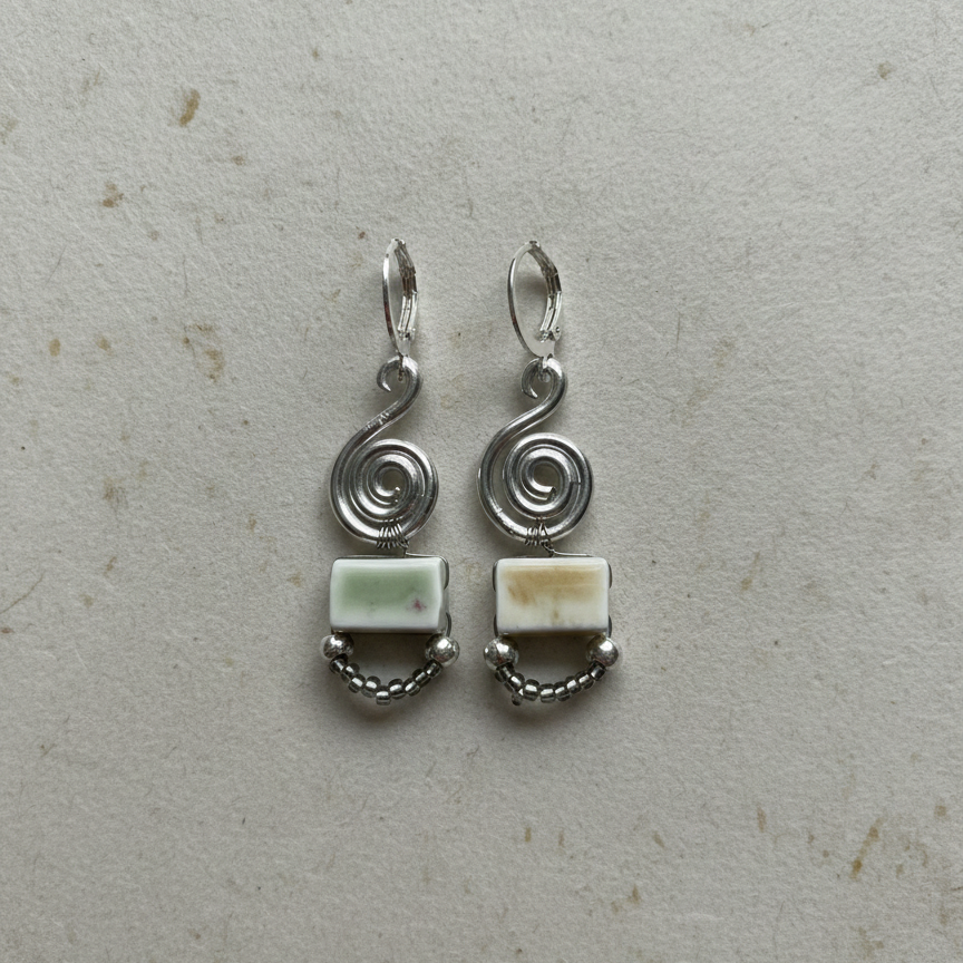 Pair of silver earrings with green stones on a textured beige background