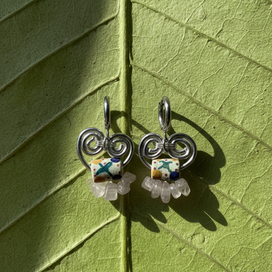Pair of silver earrings with colorful beads on a green leaf