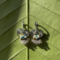 Pair of silver earrings with colorful beads on a green leaf