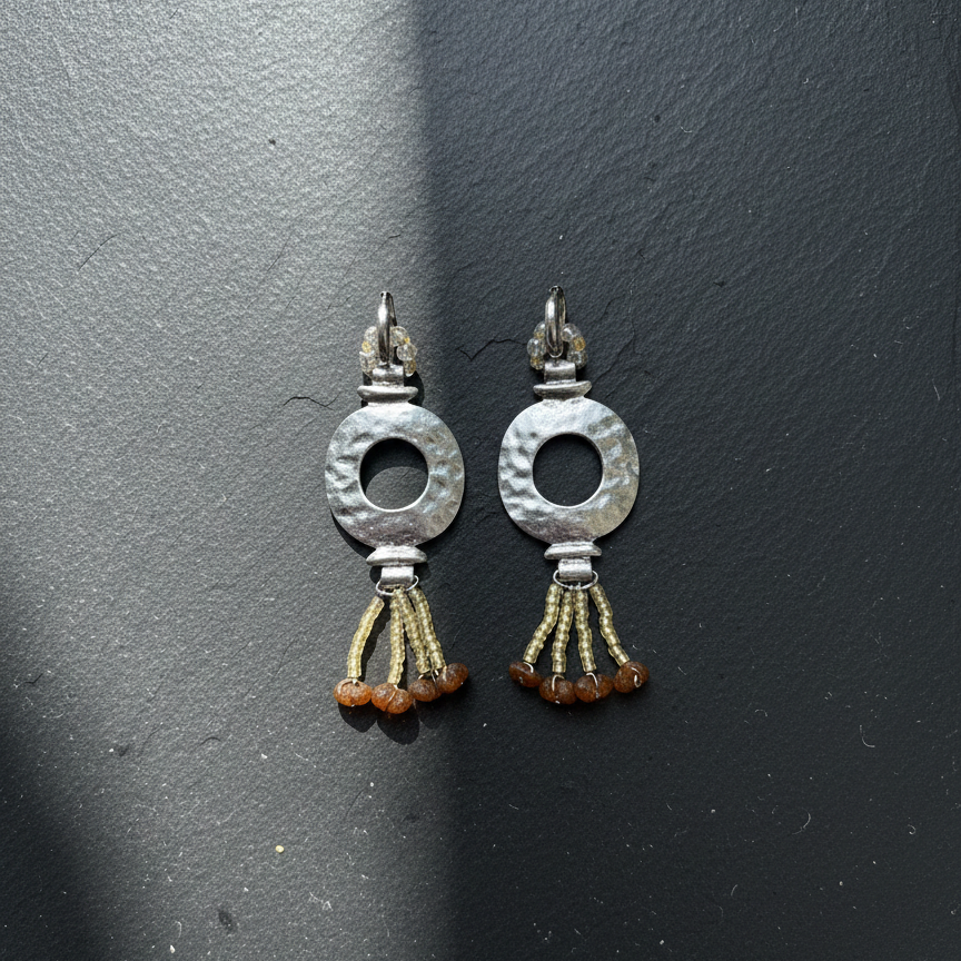 Pair of silver earrings with circular designs and orange beads on a dark gray background