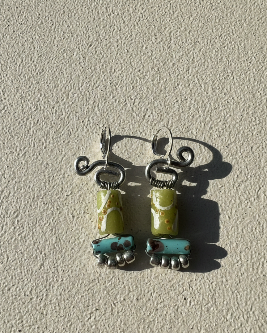 Pair of earrings with green and blue ceramic beads on a textured beige background