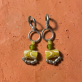 Pair of earrings with marbled green and white beads on a textured orange background