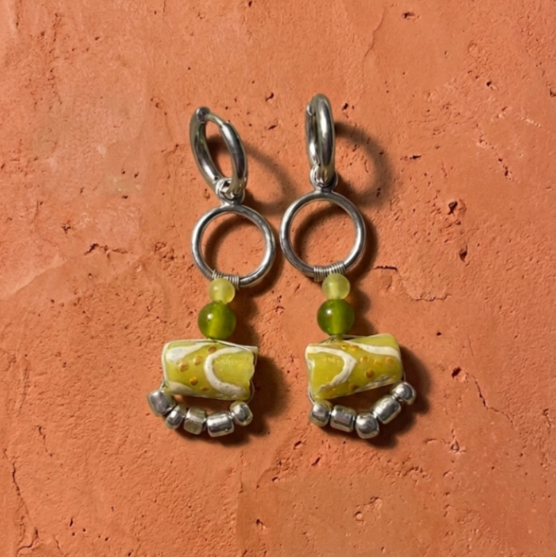 Pair of earrings with marbled green and white beads on a textured orange background