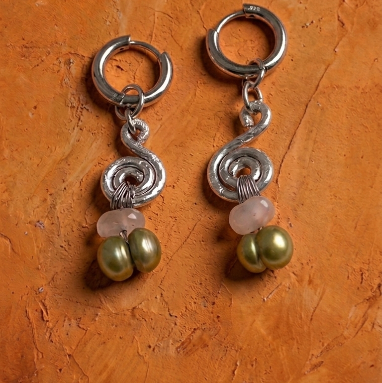 Pair of silver earrings with green beads on an orange textured background