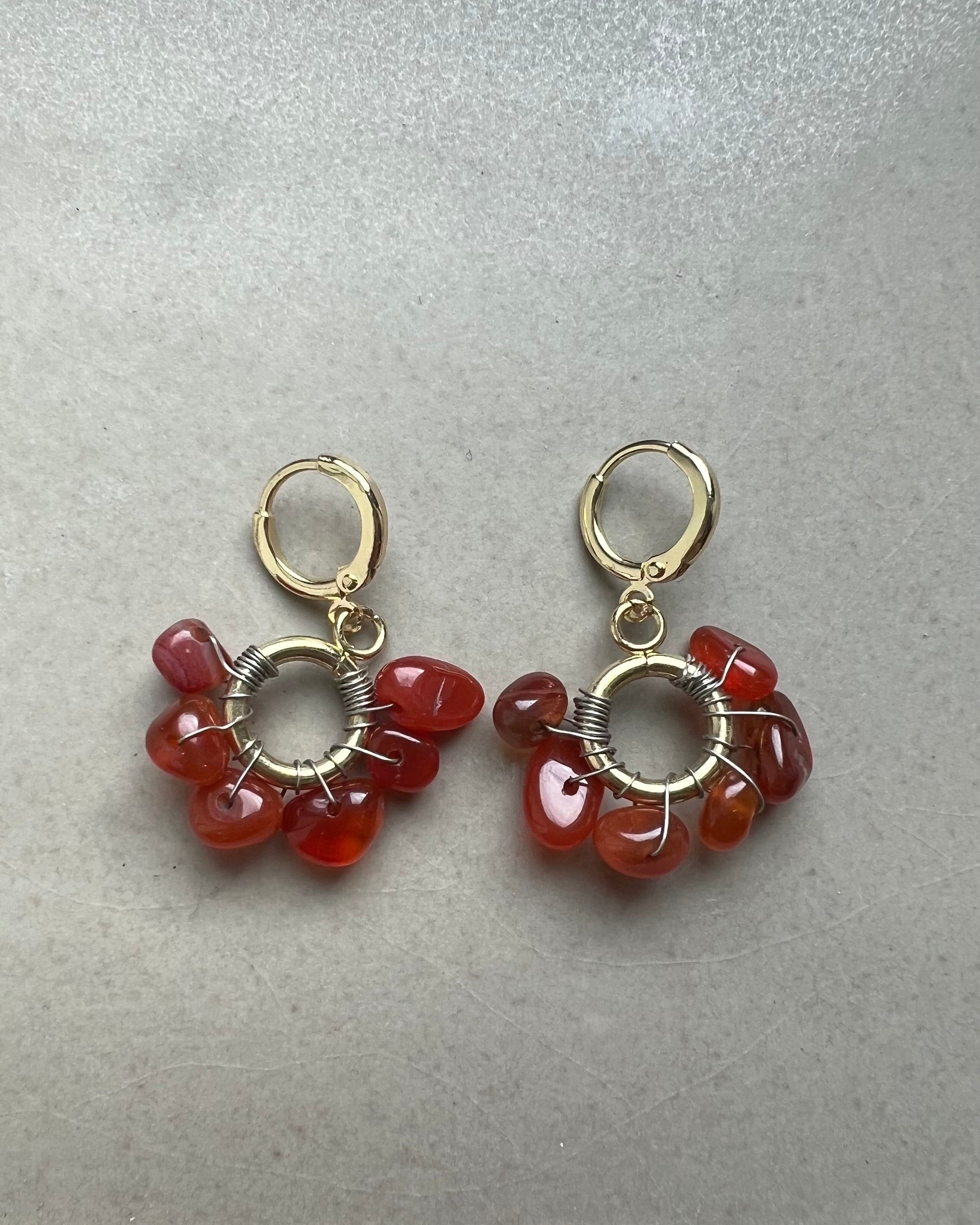 Pair of red gemstone earrings with gold loops on a gray background