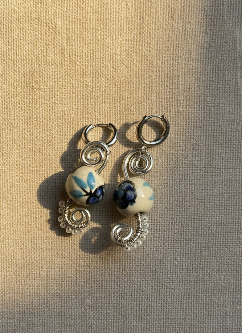 Pair of earrings with ceramic beads on a textured beige surface