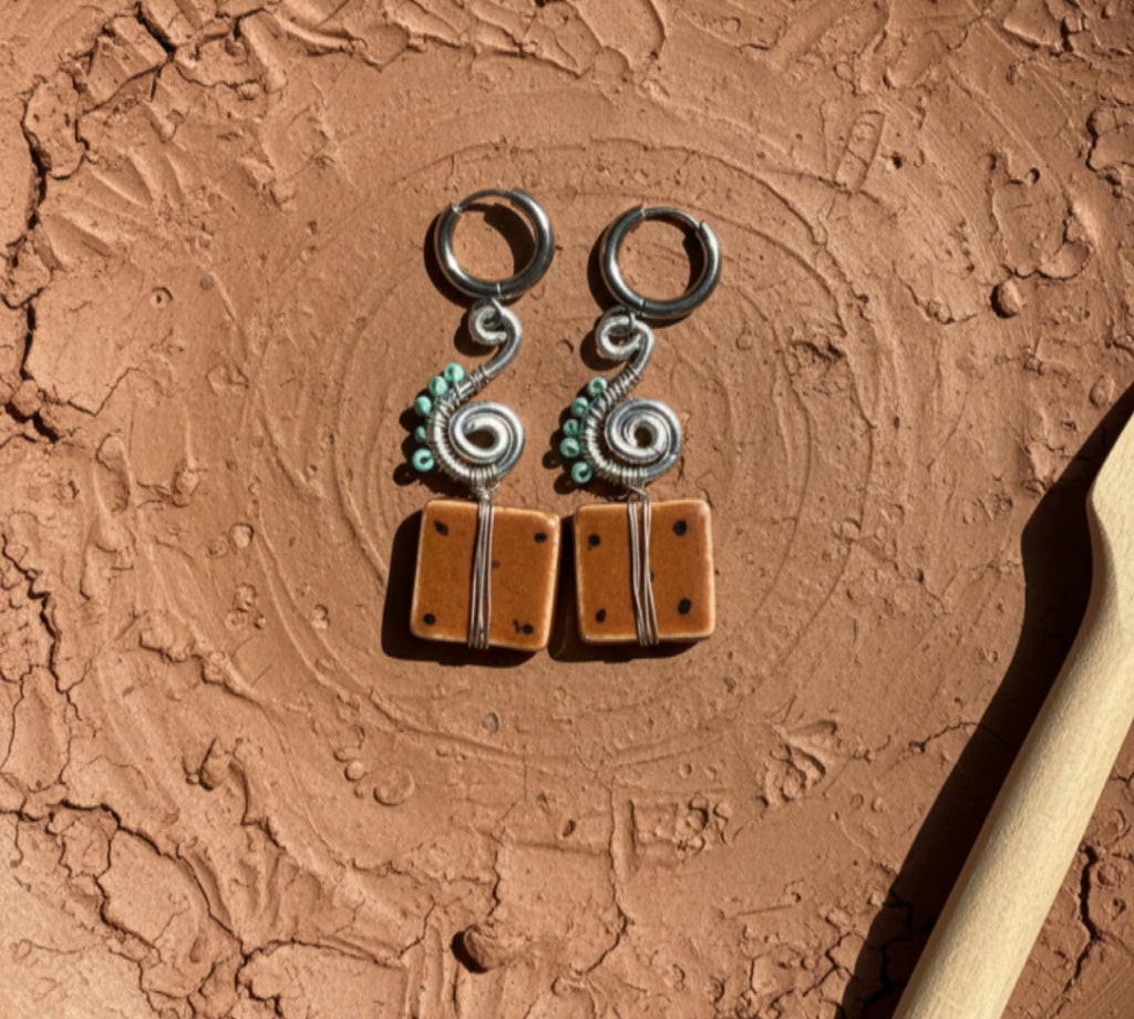 Pair of silver and brown earrings on a textured brown surface with a wooden tool.