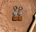 Pair of silver and brown earrings on a textured brown surface with a wooden tool.