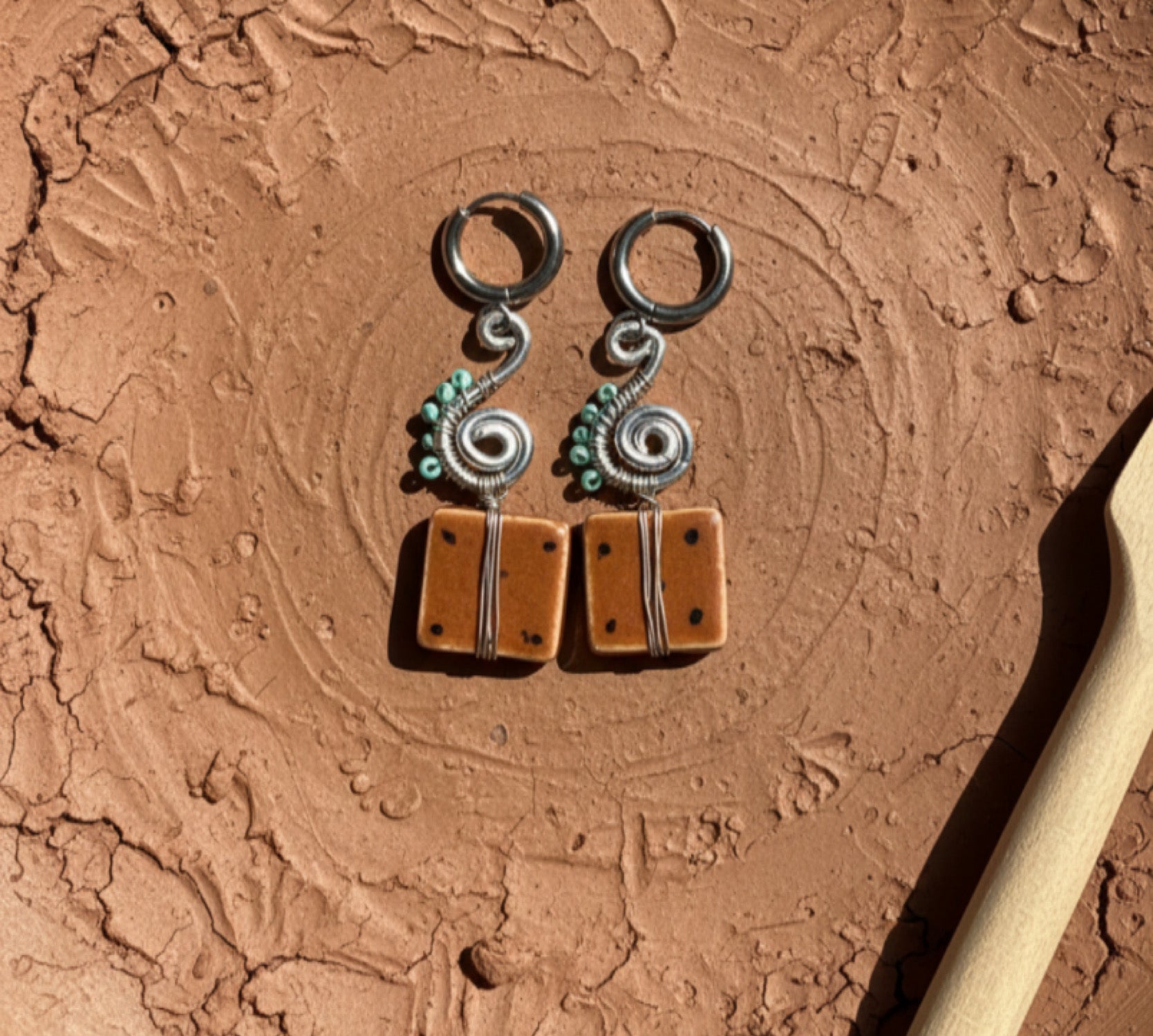 Pair of silver and brown earrings on a textured brown surface with a wooden tool.