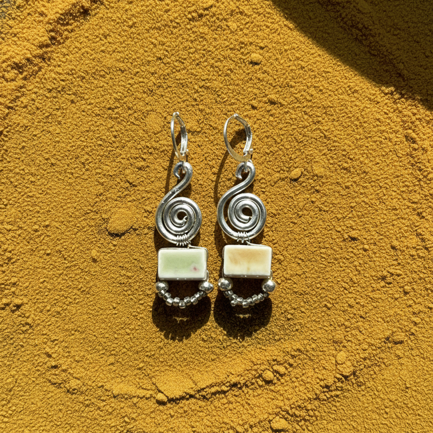 Pair of silver earrings with square stones on a textured yellow background