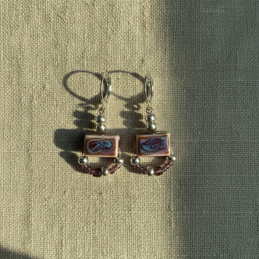 Pair of earrings with square designs on a textured fabric background